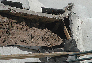 A slumped adobe wall under a concrete slab roof and behind Portland plaster at Isleta Pueblo Church, 2010.